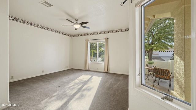 empty room with carpet floors, a ceiling fan, visible vents, and baseboards