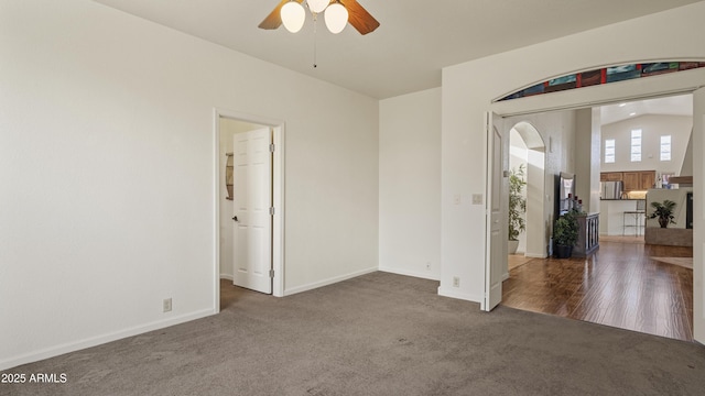 empty room with lofted ceiling, dark colored carpet, a ceiling fan, and baseboards