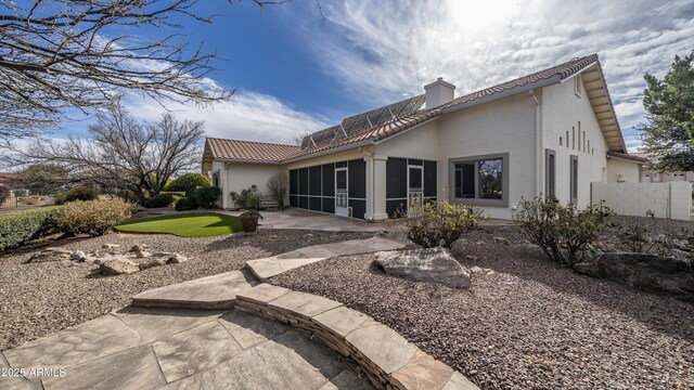 rear view of property featuring a sunroom, a tile roof, a chimney, a patio area, and stucco siding