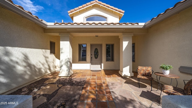 view of exterior entry featuring a patio area, a tiled roof, and stucco siding