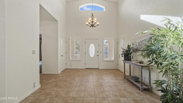 foyer with a notable chandelier, light tile patterned floors, visible vents, a towering ceiling, and baseboards