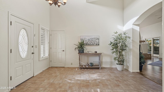 foyer entrance featuring arched walkways, a chandelier, a towering ceiling, and baseboards