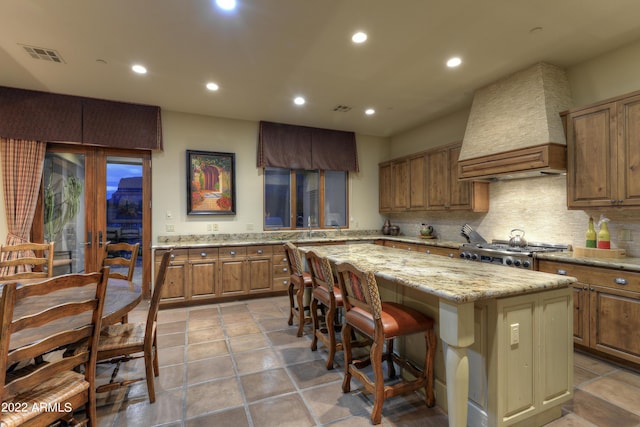 kitchen featuring premium range hood, light stone counters, a kitchen breakfast bar, a kitchen island, and stove