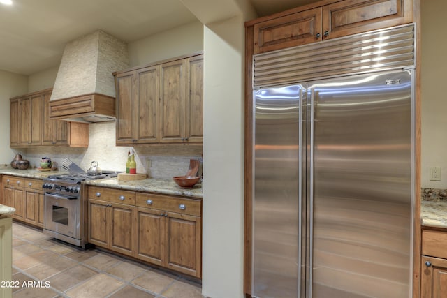 kitchen featuring light stone countertops, custom range hood, premium appliances, and decorative backsplash