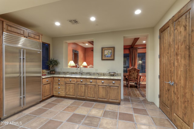 kitchen featuring light stone counters, sink, built in fridge, and light tile patterned floors