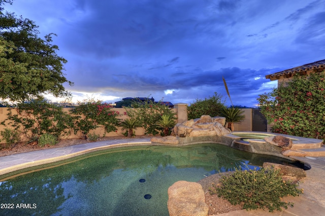 pool at dusk with an in ground hot tub