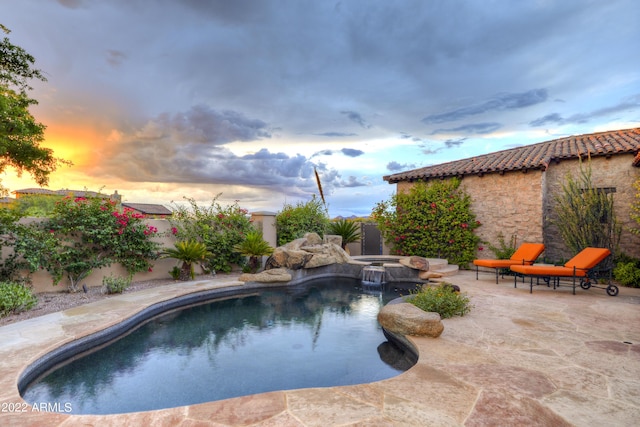 pool at dusk featuring a patio area and an in ground hot tub