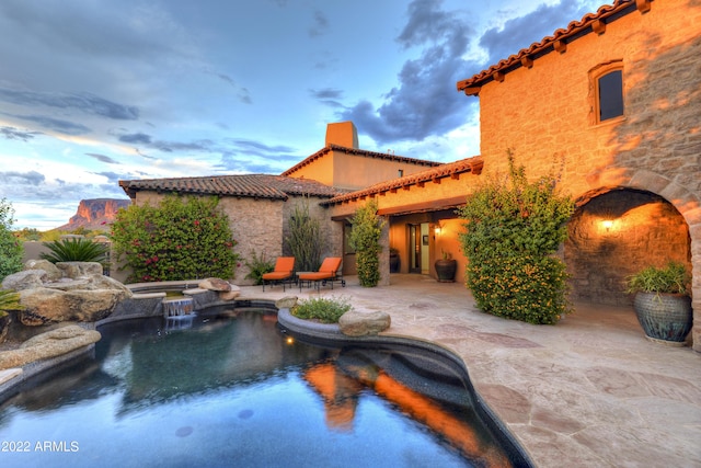 pool at dusk featuring an in ground hot tub and a patio