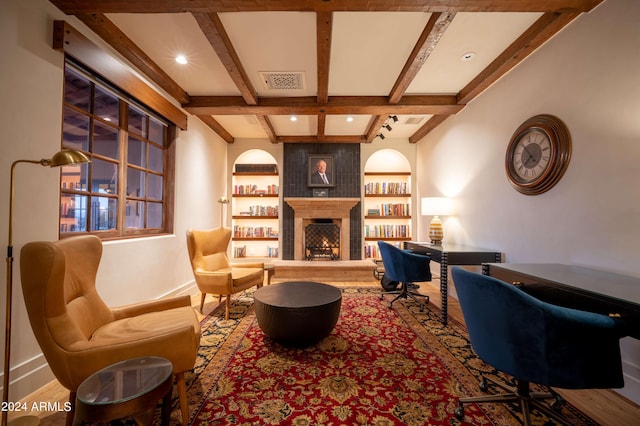 sitting room with beamed ceiling, a large fireplace, built in features, and hardwood / wood-style flooring