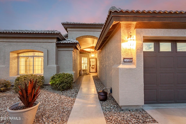 view of exterior entry featuring stucco siding, a tile roof, and a garage