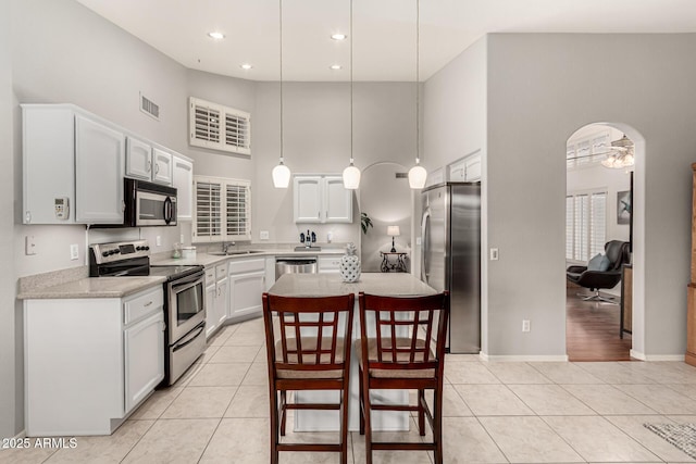 kitchen with visible vents, a kitchen island, stainless steel appliances, arched walkways, and light tile patterned flooring