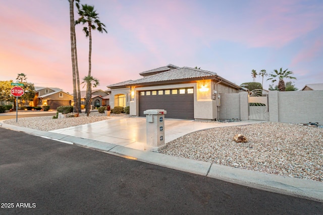 view of front facade with a gate, an attached garage, stucco siding, concrete driveway, and a tiled roof