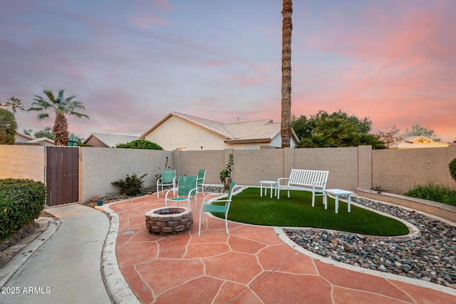 patio terrace at dusk featuring a gate, a yard, a fenced backyard, and an outdoor fire pit