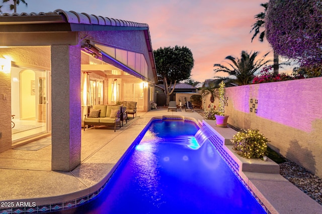 pool at dusk featuring outdoor lounge area, a patio area, a fenced in pool, and a fenced backyard