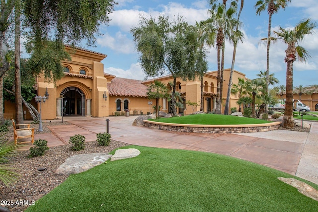 exterior space featuring curved driveway, a tile roof, a front lawn, and stucco siding