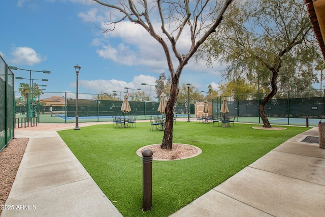 view of property's community with a tennis court, fence, and a lawn