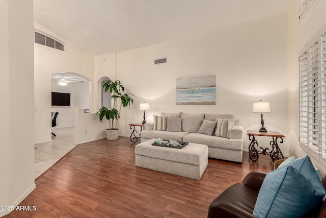 living area featuring a ceiling fan, wood finished floors, visible vents, high vaulted ceiling, and arched walkways