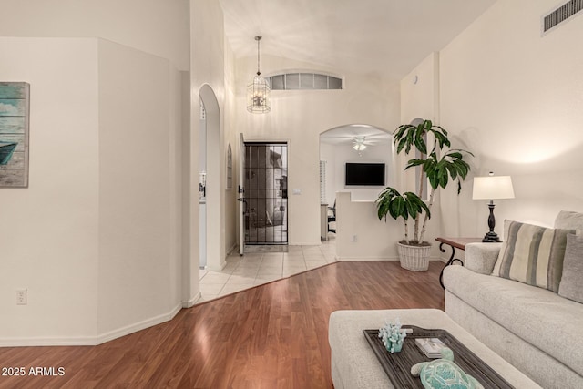 living room with baseboards, visible vents, arched walkways, a towering ceiling, and light wood-type flooring