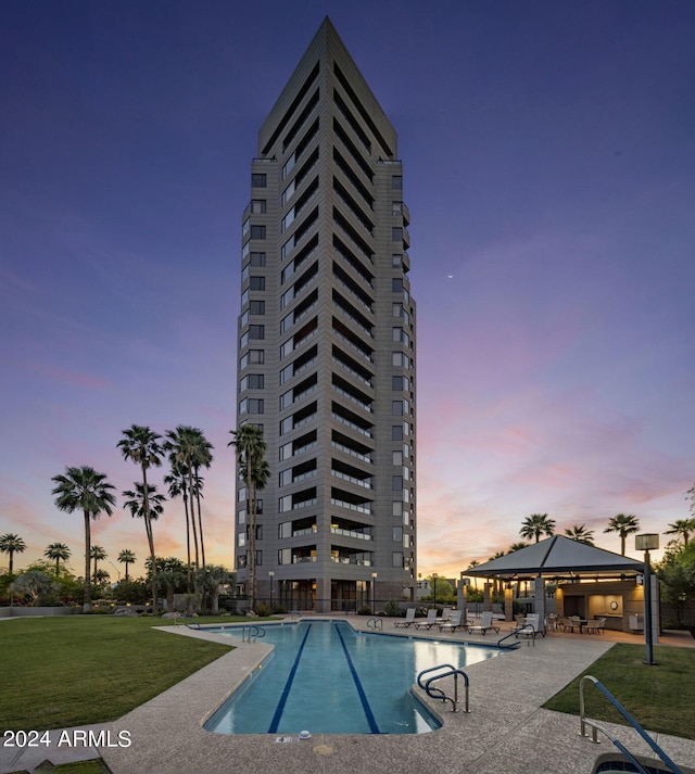 pool at dusk featuring a patio, a lawn, and a gazebo