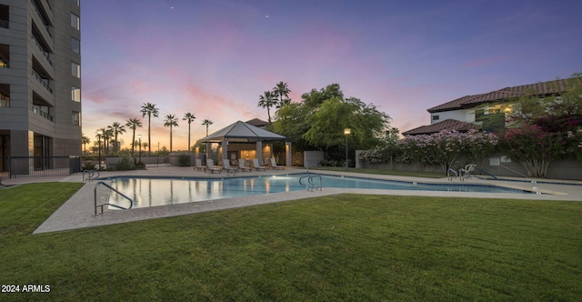 pool at dusk with a yard and a gazebo