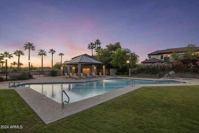 pool at dusk with a yard and a gazebo