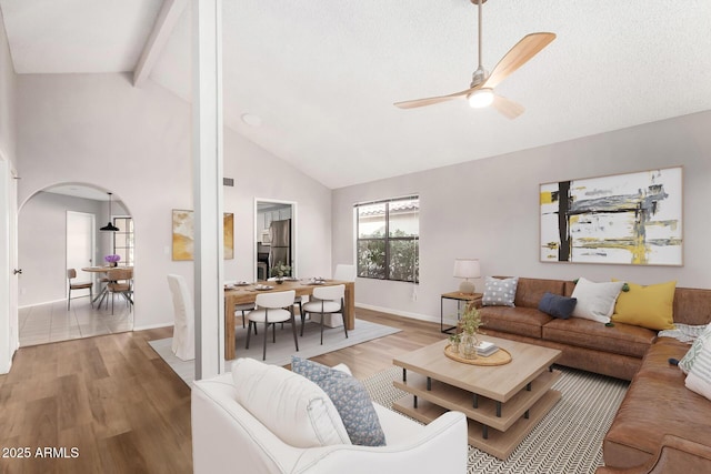 living room featuring high vaulted ceiling, beam ceiling, light hardwood / wood-style floors, and ceiling fan