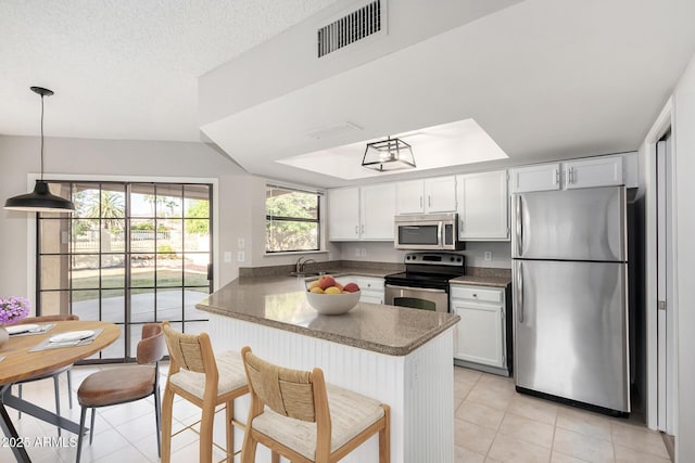 kitchen with a breakfast bar, appliances with stainless steel finishes, white cabinets, decorative light fixtures, and kitchen peninsula