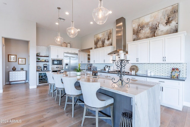 kitchen featuring white cabinetry, built in appliances, island exhaust hood, pendant lighting, and light wood-type flooring