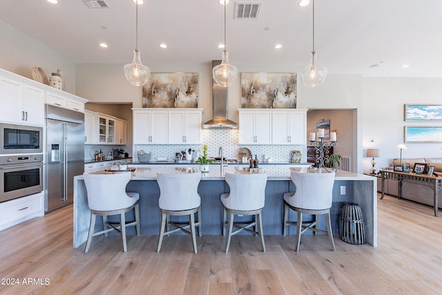 kitchen with built in appliances, decorative light fixtures, white cabinetry, and a large island with sink