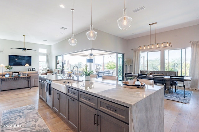 kitchen with a wealth of natural light, sink, an island with sink, and light stone counters