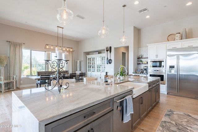 kitchen featuring sink, built in appliances, an island with sink, light hardwood / wood-style floors, and white cabinets