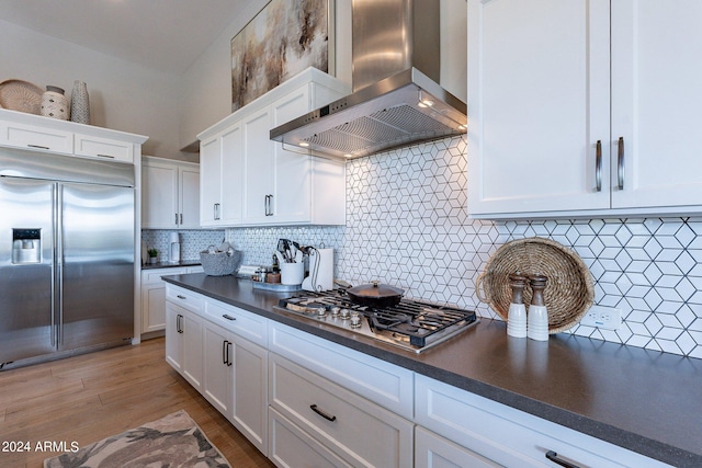 kitchen featuring tasteful backsplash, stainless steel appliances, wall chimney range hood, light hardwood / wood-style flooring, and white cabinets