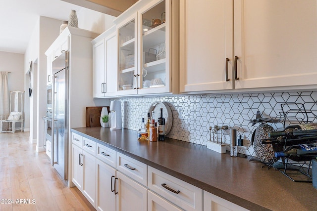 kitchen with backsplash, white cabinetry, stainless steel built in refrigerator, and light wood-type flooring