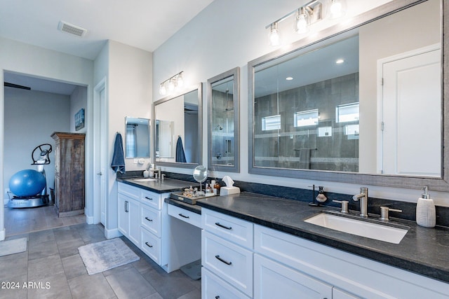 bathroom featuring tile patterned flooring, a tile shower, and vanity