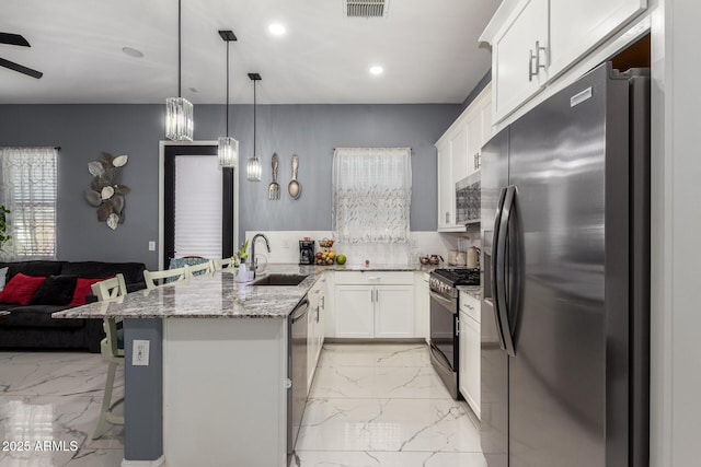 kitchen with sink, white cabinetry, stainless steel appliances, a kitchen bar, and decorative light fixtures