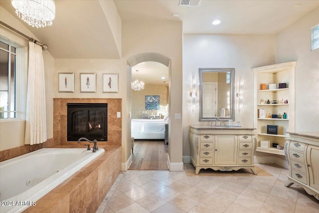 bathroom with tile patterned flooring, vanity, tiled tub, and an inviting chandelier