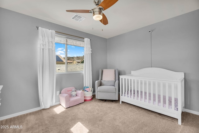 carpeted bedroom with a crib, a ceiling fan, visible vents, and baseboards