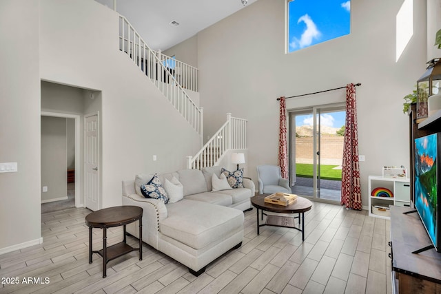 living area featuring stairway, wood finish floors, a towering ceiling, and baseboards