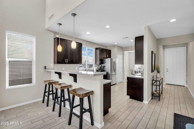 kitchen featuring a kitchen breakfast bar, freestanding refrigerator, light countertops, dark brown cabinets, and wood finish floors