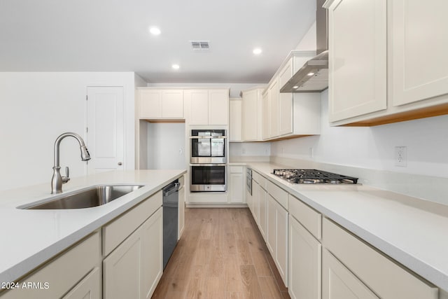 kitchen featuring sink, wall chimney exhaust hood, light hardwood / wood-style floors, white cabinetry, and stainless steel appliances