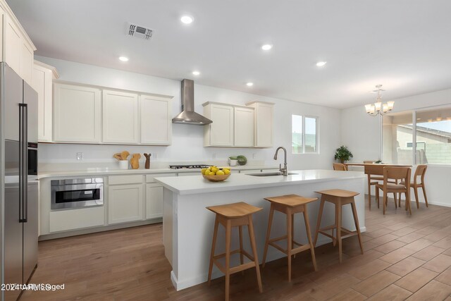 kitchen featuring a center island with sink, sink, wall chimney range hood, and white cabinets