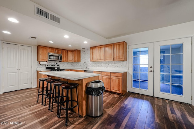 kitchen with sink, a breakfast bar area, appliances with stainless steel finishes, dark hardwood / wood-style floors, and a kitchen island