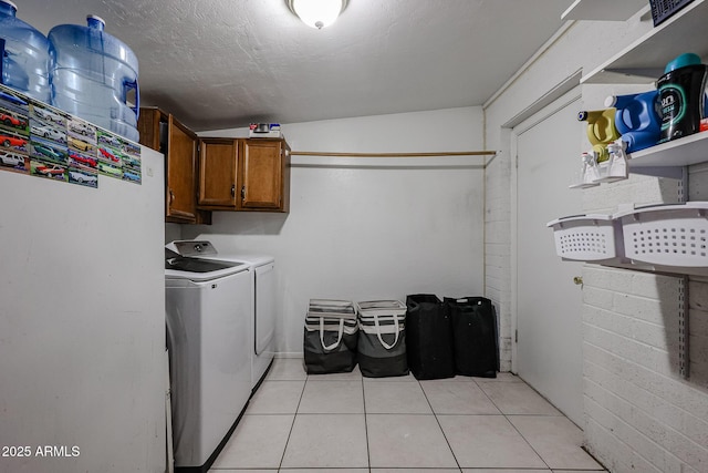 laundry area featuring washing machine and dryer, cabinets, a textured ceiling, and light tile patterned flooring