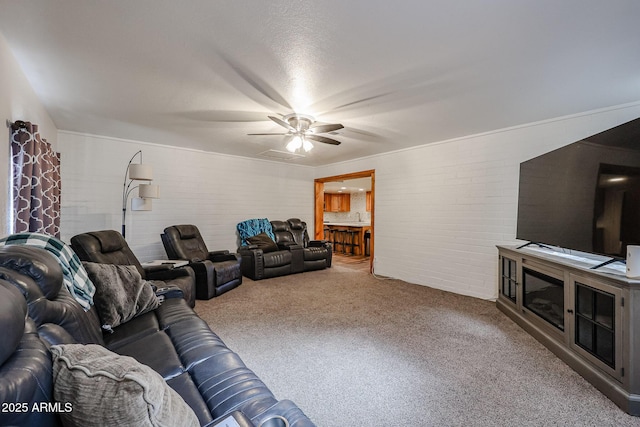 carpeted living room featuring ceiling fan and brick wall