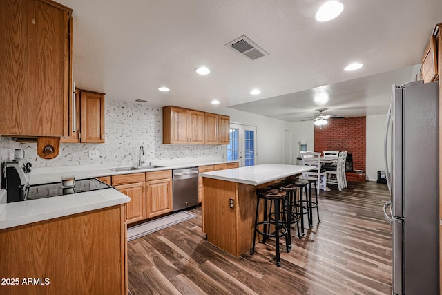 kitchen with a kitchen island, a breakfast bar, appliances with stainless steel finishes, sink, and dark hardwood / wood-style flooring