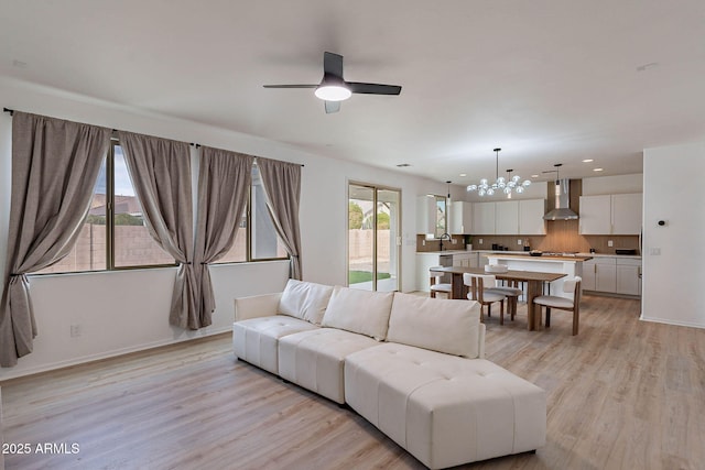 living room featuring light wood-style flooring, ceiling fan with notable chandelier, baseboards, and recessed lighting