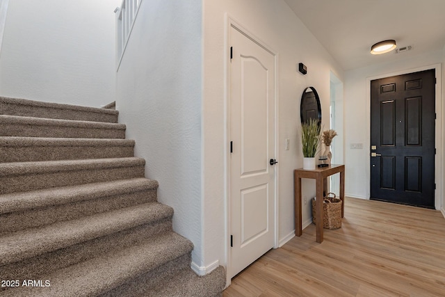 foyer entrance with stairway, light wood-type flooring, visible vents, and baseboards