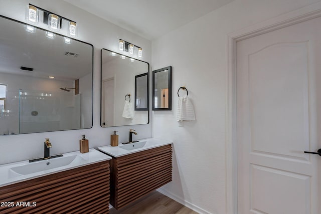 full bath featuring two vanities, visible vents, a stall shower, a sink, and wood finished floors