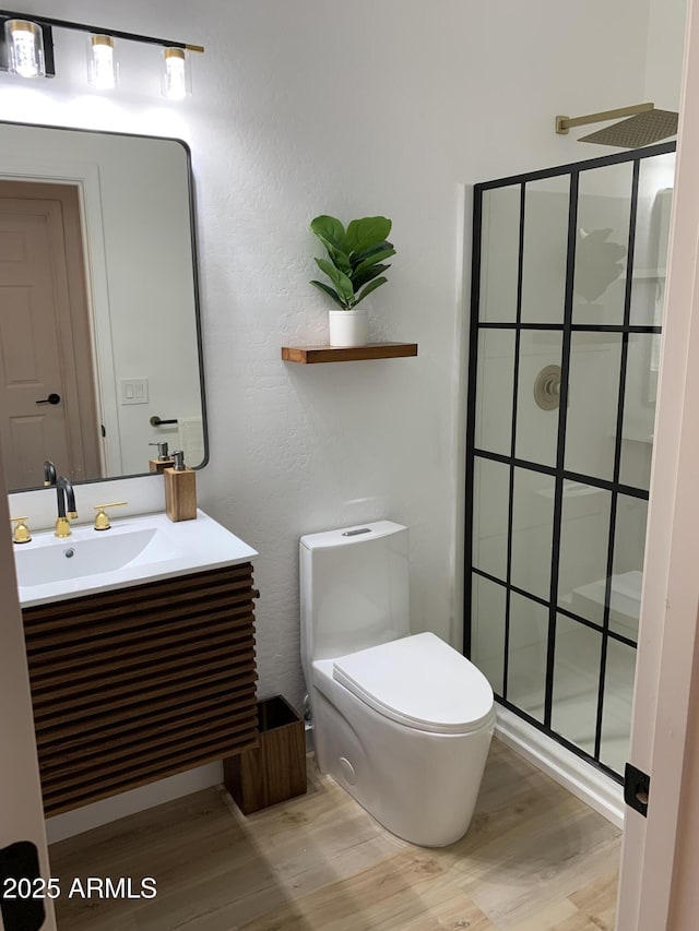 bathroom featuring a walk in shower, vanity, wood finished floors, and toilet