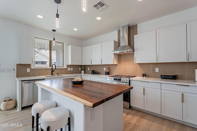 kitchen with stainless steel appliances, a sink, wooden counters, wall chimney range hood, and tasteful backsplash